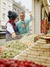 A young couple are standing in front of a shop window filled with colorful sweets. The woman on the left is wearing a furry hat and a blue vest, while the man on the right, dressed in a blue sweater and sunglasses on their head, is pointing at the sweets inside. There is a street scene in the background.