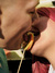 A close-up shot of a young couple licking a large, colorful lollipop. The shot captures their faces in profile, emphasizing the lollipop between them. The woman on the right has vibrant red hair.