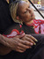 A close-up of a woman with blonde braids resting peacefully on her partner's lap. The woman is wearing a red, pink and black patterned top, and her eyes are closed, with a calm and content expression on her face.