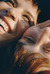 A close-up shot of a young couple smiling closely together. The image captures the joy in their expressions, with the light highlighting their faces. Their heads are touching, and the mood is one of warmth and affection.